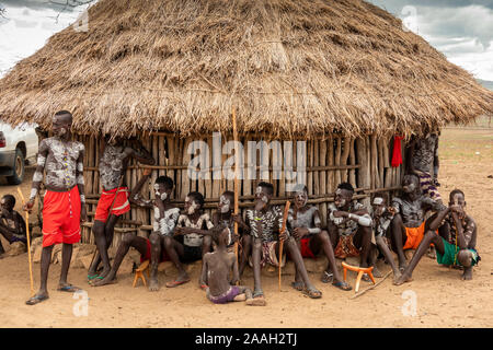 L'Éthiopie, de l'Omo, Kolcho village, habillé traditionnellement les hommes des tribus Karo assis dans l'ombre de hut eaves Banque D'Images