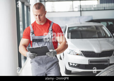 Un beau jeune homme parle à un concessionnaire d'automobiles, réparation d'une voiture dans un atelier. Banque D'Images