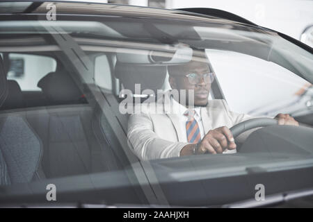 Vue avant du beau élégant africain des affaires sérieuses homme conduit une voiture Banque D'Images