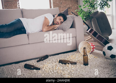 Photo de boozer multiethnique boissons guy couché couchage canapé bière gueule de bouteilles vides du popcorn marbre souffrances après bachelor party matin messy Banque D'Images