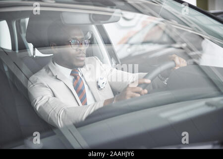 Vue avant du beau élégant africain des affaires sérieuses homme conduit une voiture Banque D'Images