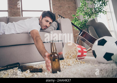 Photo de race mixte boozer guy couché canapé en tenant la bouteille de bière du popcorn sur plancher avait divertissement folles souffrances après partie hangover matin maux de tête Banque D'Images