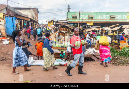 L'Afrique de l'homme portant une paire de gros melons à un marché alimentaire en bordure d'occupation dans un village près de Kampala, Ouganda, Région du Centre Banque D'Images