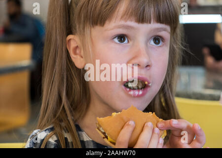 Joli enfant girl eating fast food in a restaurant. Banque D'Images