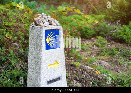 Le jaune coquille Saint-Jacques, symbole touristique du Camino de Santiago direction montrant sur Camino Norte en Espagne.Colonne avec la signature de la façon de roches Banque D'Images