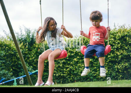 Soeur et frère cadet de balançoires dans le jardin Banque D'Images