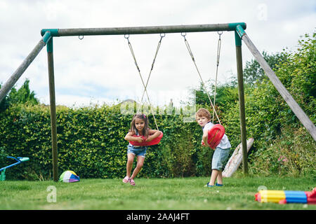 Fille et garçon se tordant autour sur des balançoires dans le jardin Banque D'Images