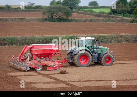 Agriculteur à l'œuvre l'ensemencement de graminées fourragères pour la nouvelle saison, à l'aide d'un semoir semoir ou à Cornwall en Angleterre. Banque D'Images