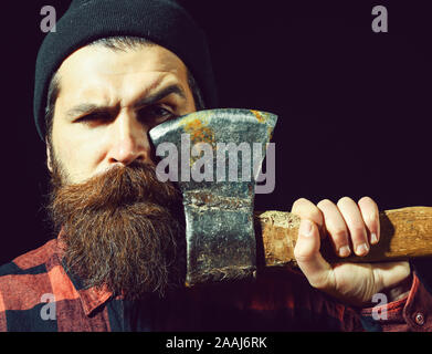 Bel homme ou bûcheron, hipster barbu avec barbe et moustache en hat détient old rusty lame de fer d'ax isolé sur fond noir Banque D'Images