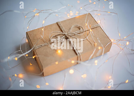 Boîte-cadeau d'artisanat du carton dans une guirlande lumineuse sur le fond blanc. Banque D'Images