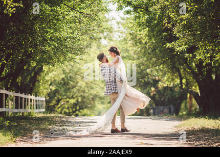 Heureux époux soulève promise au parc d'été. homme et femme d'accolade a soulevé ses bras. Nouvelle couple dans le parc. Juste mariés. Promenade dans le parc Banque D'Images