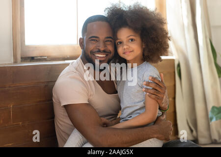 Smiling dad biracial et bambin fille hug looking at camera Banque D'Images