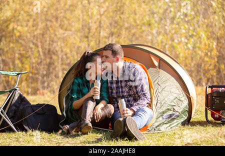 Jeune couple amoureux de thermos dans la main s'embrasser devant la tente. Couple heureux en vacances Banque D'Images