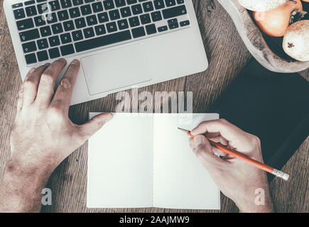 Vue de dessus de l'homme en prenant des notes sur l'application notes tout en travaillant sur un ordinateur portable sur la table en bois Banque D'Images