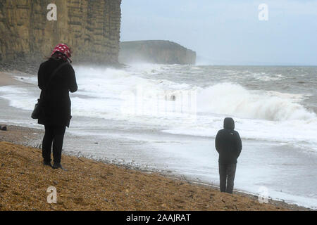 West Bay, Dorset, UK. 22 novembre 2019. Météo britannique. Une femme et un homme sur la plage en regardant la mer difficile crash à terre de West Bay, dans le Dorset après une matinée de pluie. Crédit photo : Graham Hunt/Alamy Live News Banque D'Images