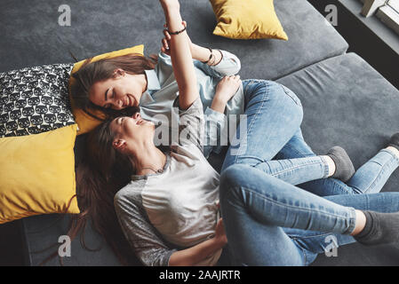 Deux soeurs jumelles cute smiling holding smartphone et décisions. selfies Les filles se coucher sur le canapé posant et la joie Banque D'Images