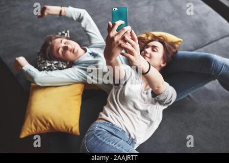 Deux soeurs jumelles cute smiling holding smartphone et décisions. selfies Les filles se coucher sur le canapé posant et la joie Banque D'Images