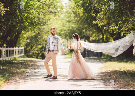 Couple de mariage belle forêt bois. Mariés, suivez-moi, couple marié, femme en robe de mariée blanche et voile. Histoire d'amour à l'extérieur rustique Banque D'Images