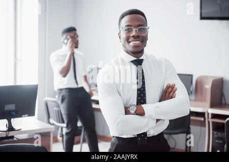 Travailler avec sourire. Heerful african businessman standing in front of collègue. Banque D'Images