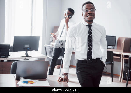 Travailler avec sourire. Heerful african businessman standing in front of collègue. Banque D'Images