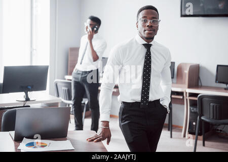 Travailler avec sourire. Heerful african businessman standing in front of collègue. Banque D'Images
