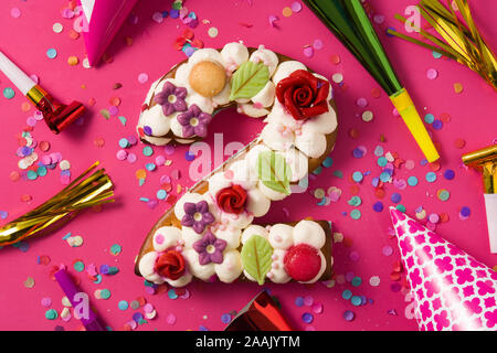 Numéro deux gâteau décoré avec des fleurs, des macarons et confettis isolé sur fond rouge Banque D'Images