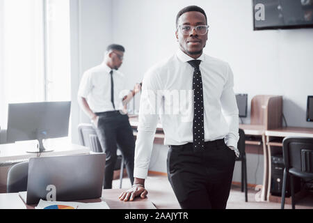 Travailler avec sourire. Heerful african businessman standing in front of collègue. Banque D'Images
