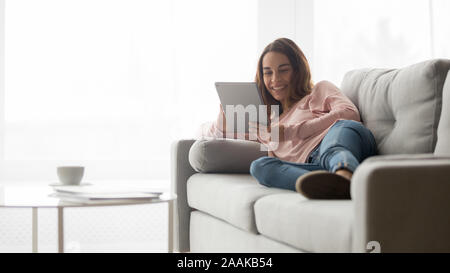 Smiling girl se détendre sur le divan regardant la vidéo sur tablette Banque D'Images