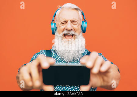 Homme barbu Senior faire avec selfies téléphone mobile lors de l'écoute de sa lecture favorite avec casques - vêtements homme mûri s'amusant Banque D'Images