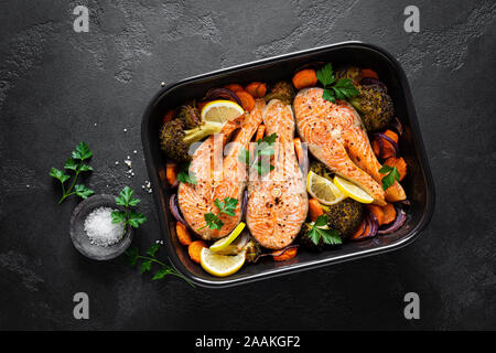 Le saumon. Darnes de saumon au four avec des légumes, le brocoli, la carotte et l'oignon sur fond noir, vue du dessus Banque D'Images