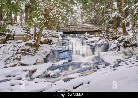 Après la première chute de neige de la saison, l'eau passe sous une passerelle et tombe sur les roches du Bouclier canadien de Potts Falls à Muskoka. Banque D'Images