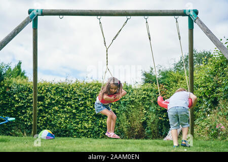 Fille et garçon se tordant autour sur des balançoires dans le jardin Banque D'Images