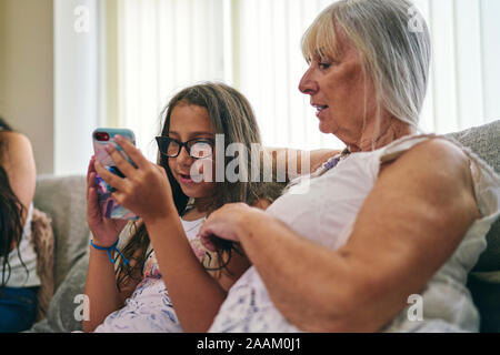 Grand-mère en regardant sa petite-fille de jouer aux jeux vidéo sur canapé Banque D'Images