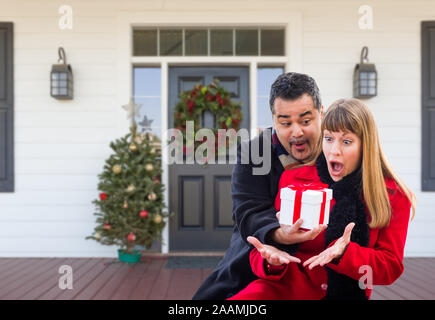 Young Mixed Race Woman l'échange de cadeau au porche de la maison avec des décorations de Noël. Banque D'Images