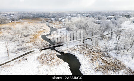 Drone / Vue aérienne d'un petit pont à travers une forêt de préserver et de traverser une rivière après une tempête de neige. Banque D'Images