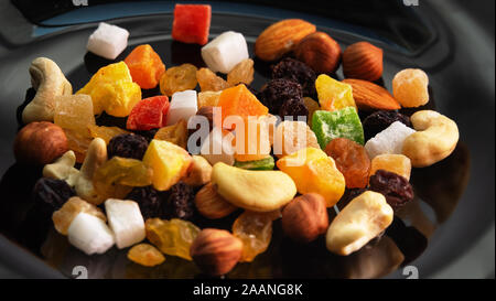 Tutti frutti. Mélange de fruits secs (raisins, citron, mangue) et les noix (amandes, noisettes) sur un plat laqué noir Banque D'Images