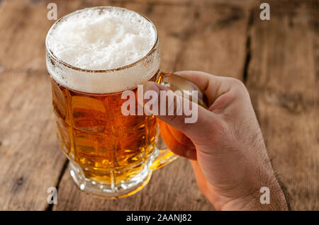 Main tenant un verre de bière blonde sur fond rustique en bois. Banque D'Images