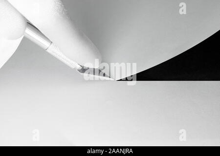 Homme avec des gants blancs la coupe du papier blanc avec cutter sur fond noir qui visibles à travers la ligne de coupe Banque D'Images