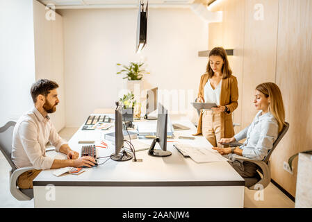 Les jeunes employés habillés à la légère de faire certains travaux de création à la grande table avec les ordinateurs dans le bureau. Concept d'une entreprise d'architecture et de création Banque D'Images