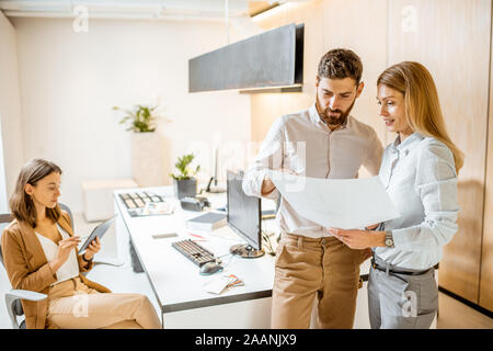 Creative office employés travaille sur des projets architecturaux, holding blueprints et travaillant à l'ordinateur dans les bureaux modernes Banque D'Images