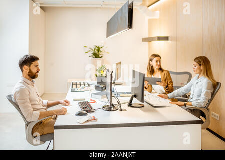 Les jeunes employés habillés à la légère de faire certains travaux de création à la grande table avec les ordinateurs dans le bureau. Concept d'une entreprise d'architecture et de création Banque D'Images