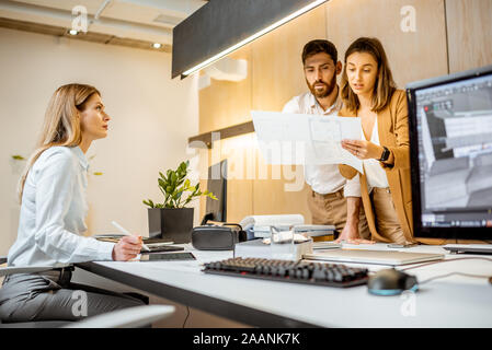 Les jeunes employés habillés à la légère de faire certains travaux de création à la grande table avec les ordinateurs dans le bureau. Concept d'une entreprise d'architecture et de création Banque D'Images