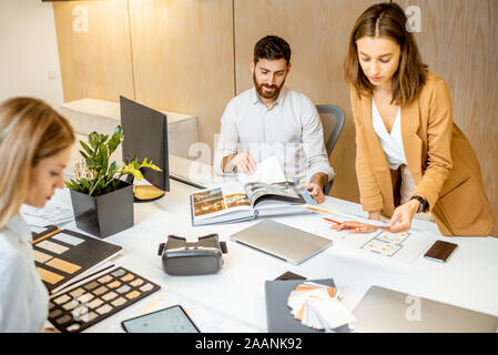 Les jeunes employés habillés à la légère de faire certains travaux de création à la grande table avec les ordinateurs dans le bureau. Concept d'une entreprise d'architecture et de création Banque D'Images