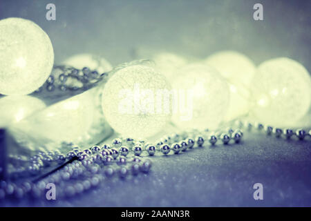 guirlande lumineuse sous forme de boules brille sur un fond argenté étincelant, à côté de perles d'argent, une copie de l'espace pour votre conception. Joyeux Noël Banque D'Images