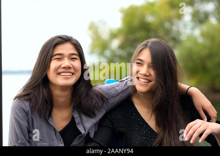 Deux soeurs métissés, Caucasien Asiatique teen girls, outdoors smiling by lake avec les bras sur les épaules Banque D'Images