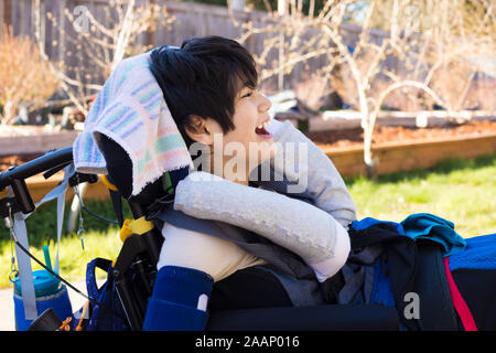 De 11 ans beau garçon biracial handicapés en fauteuil roulant assis en plein air sur une journée d'été, smiling Banque D'Images