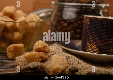 Morceaux de sucre brun dans un sucrier, une tasse de café, grains de café sur un fond de bois. Close up Banque D'Images