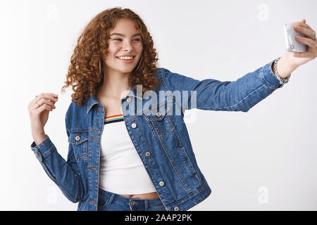 Carefree smiling cute jeune fille rousse de rousseur bouclés en tenant le bras d'extension selfies tenir posant souriant smartphone téléphone appareil d'oeil amusé optimiste Banque D'Images