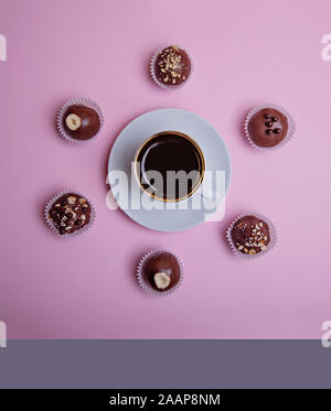 Une tasse de café expresso sur une soucoupe et 6 chocolats sur un fond rose. Vue de dessus. Banque D'Images