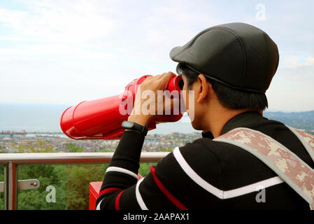 Jeune homme l'observation d'Aerial Vue sur la ville avec des jumelles à partir de la plate-forme d'observation Banque D'Images